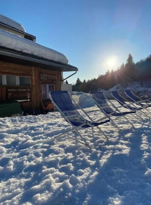 Edificio de madera con un cartel que dice 'Scuola Italiana', rodeado de nieve y sillones azules.