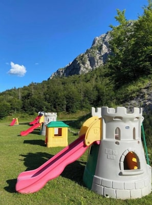 Un parque infantil con una estructura de castillo, toboganes y un telón de fondo montañoso.