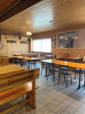 A restaurant with wooden walls, tiled floor, and tables with chairs.