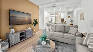A living room with a flat-screen TV, grey sofa, and a coffee table with a plant. - Lucaya Luxe At Bahama Bay (Davenport)