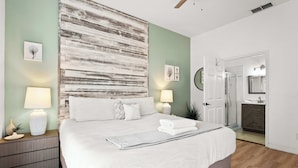 A bedroom with a large bed, bedside lamps, a nightstand, a wall art piece, and a door leading to a bathroom. - Lucaya Luxe At Bahama Bay (Davenport)