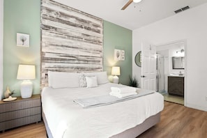 A bedroom with a large bed, bedside lamps, a nightstand, a wall art piece, and a door leading to a bathroom. - Lucaya Luxe At Bahama Bay (Davenport)