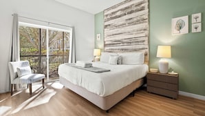 A bedroom with a large bed, a chair, a nightstand, and a view of the outdoors. - Lucaya Luxe At Bahama Bay (Davenport)