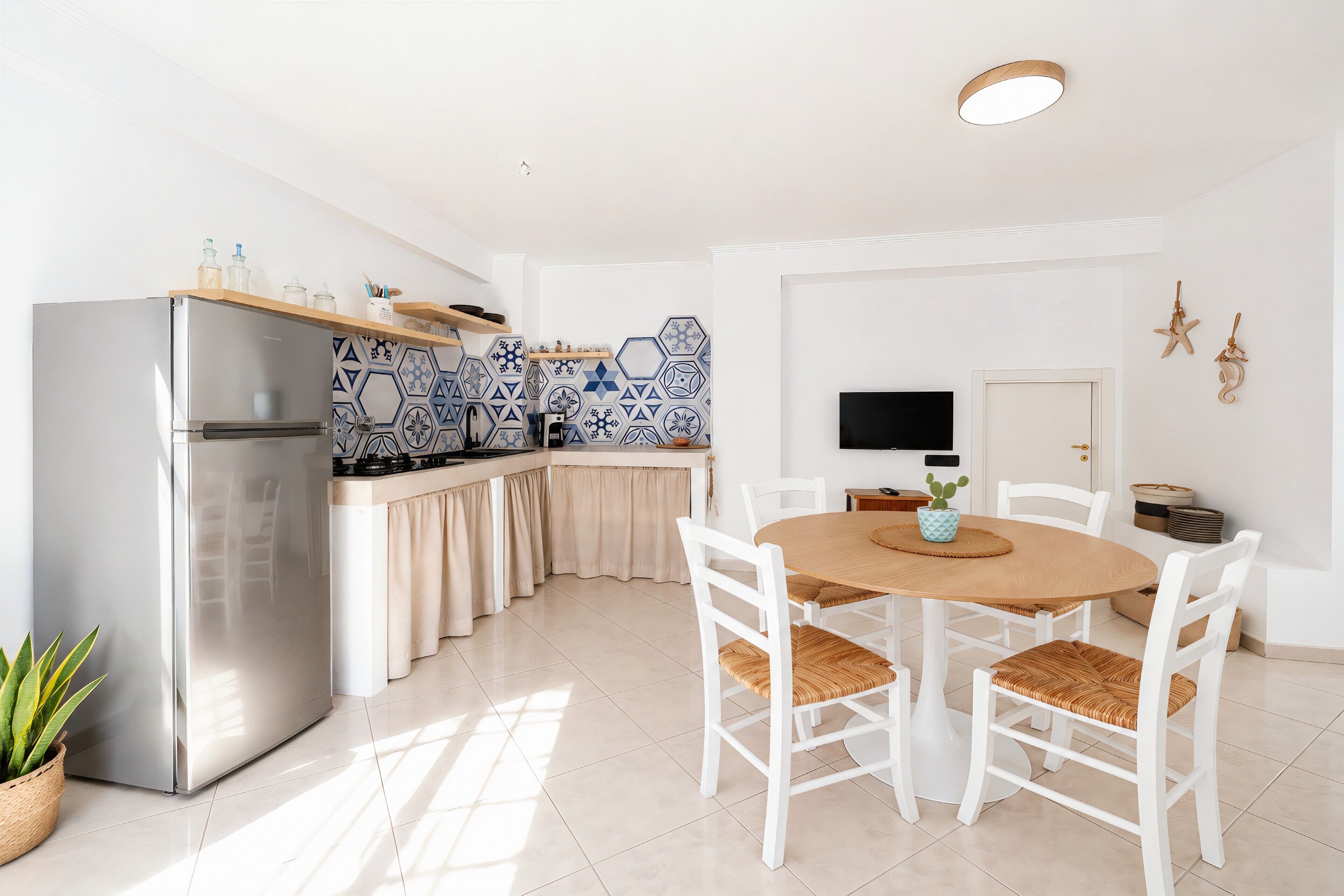 Una cocina moderna con refrigerador empotrado, muebles blancos y un comedor con mesa redonda de madera y sillas blancas.