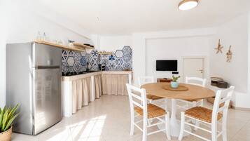 Una cocina moderna con refrigerador empotrado, muebles blancos y un comedor con mesa redonda de madera y sillas blancas.