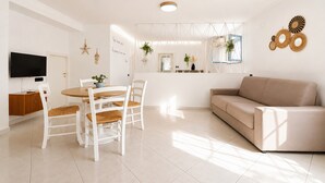 Een moderne woonkamer met een beige bank, witte stoelen, een eettafel en een televisie.