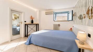 A bedroom with a bed, bedside table, lamp, window, radiator, and a door with a glass panel.