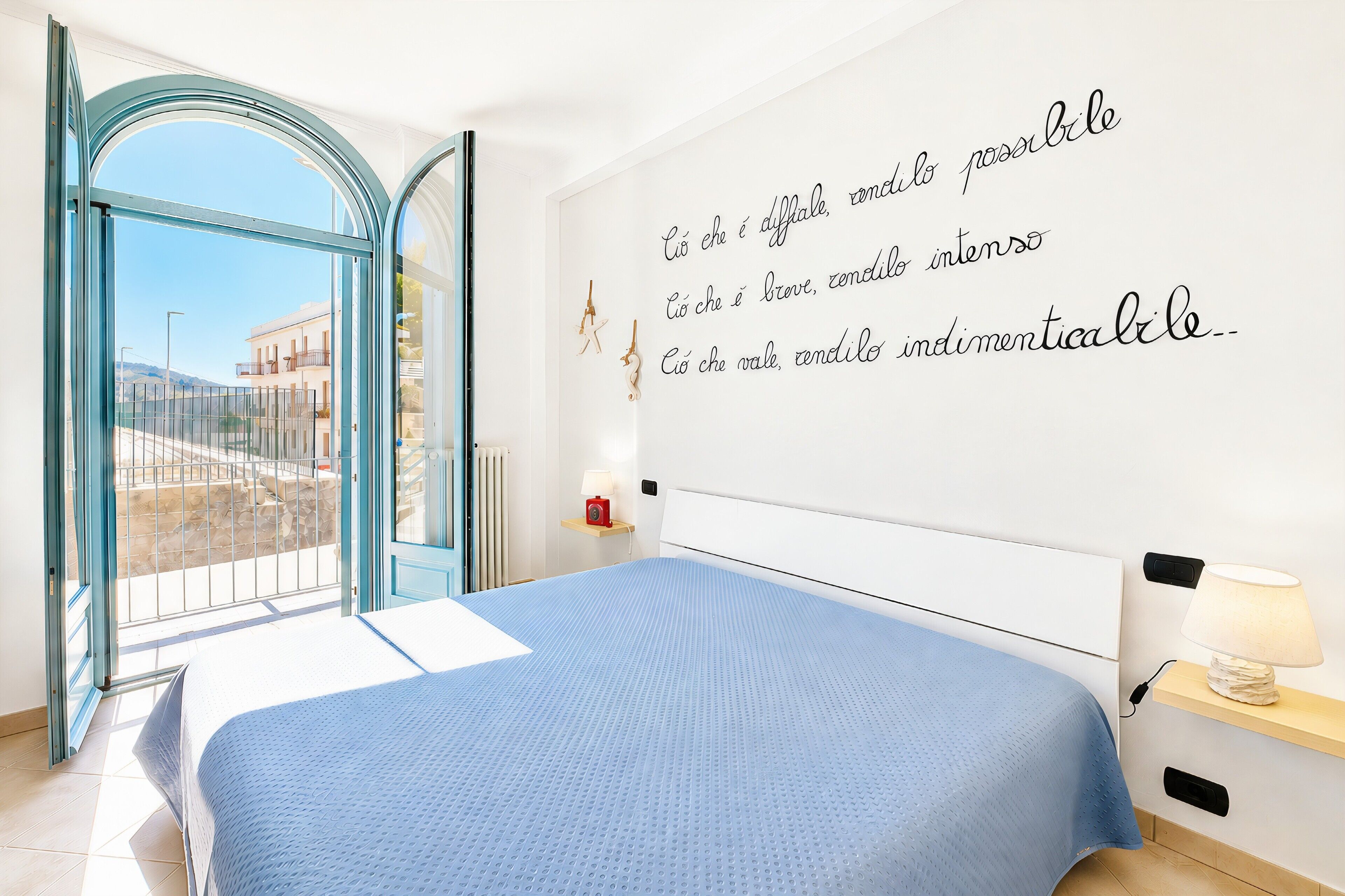 Een slaapkamer met een bed, een raam, een muur met tekst en een nachtkastje met een lamp.