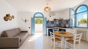 Een moderne keuken met blauwe en witte tegels, een eethoek met een houten tafel en witte stoelen, en een beige bank.