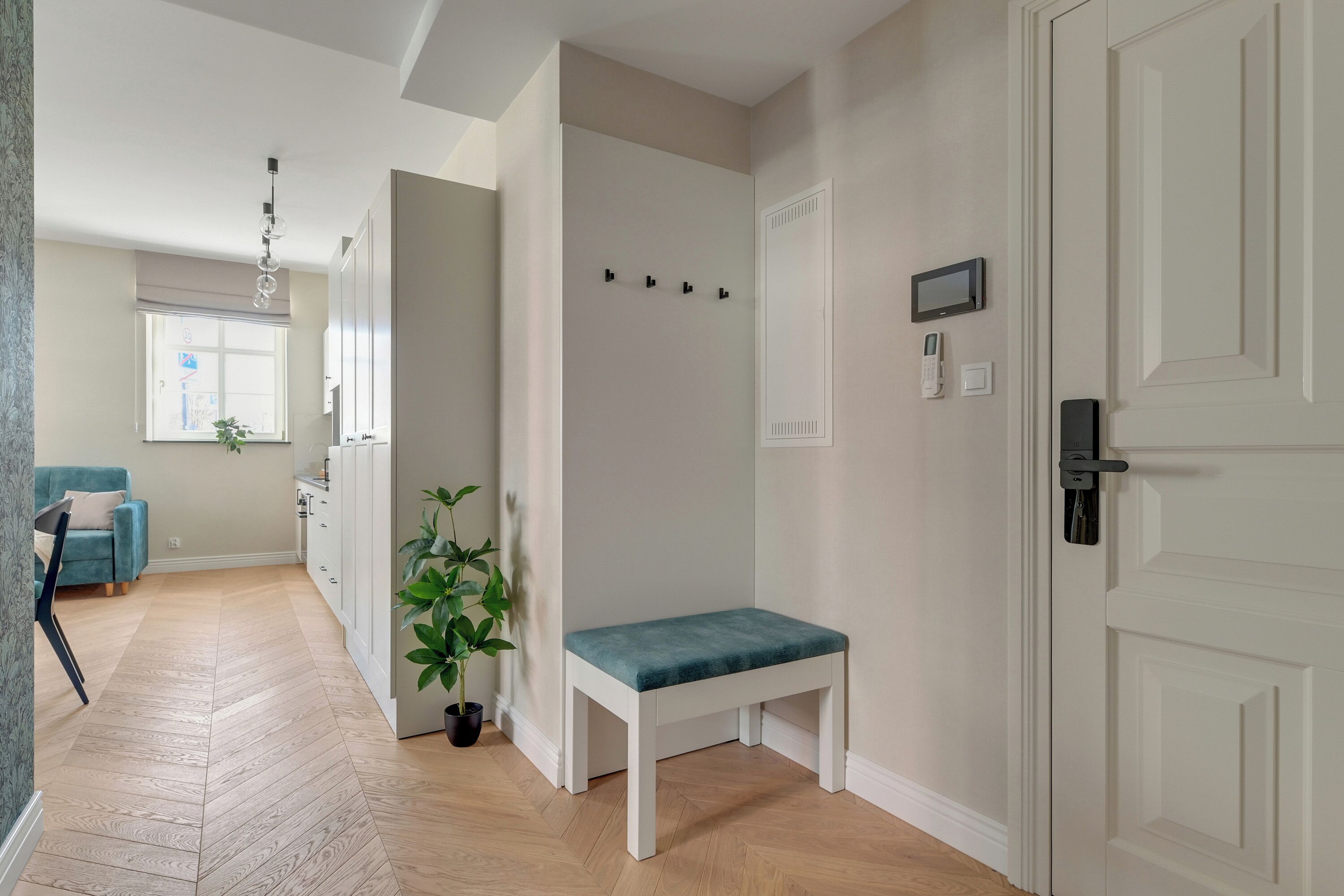 A hallway with a bench, a door, a coat rack, a plant, and a window.
