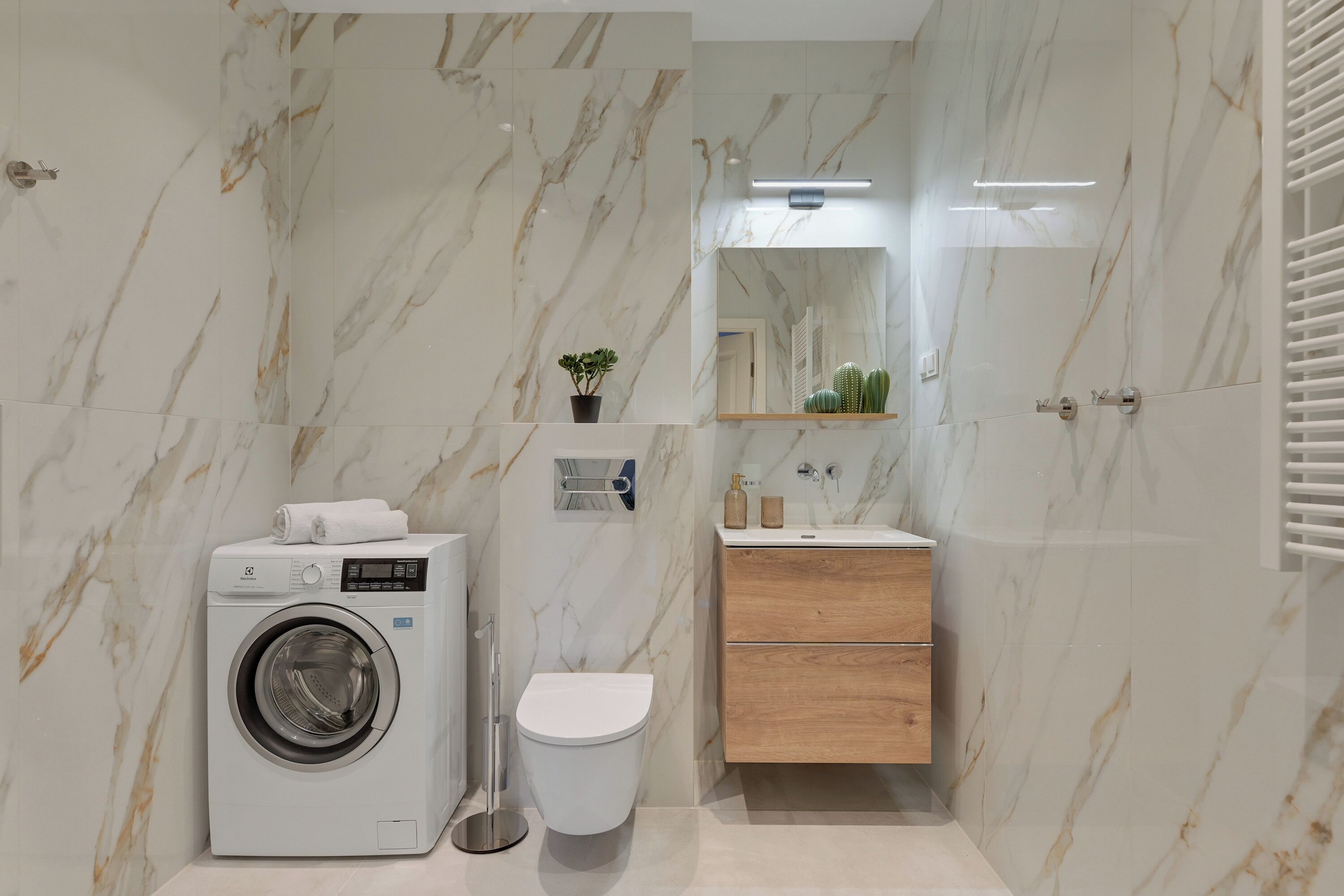 A compact bathroom with a washing machine, toilet, and wooden vanity.