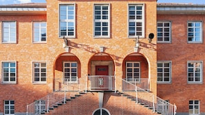 Ein Gebäude aus roten Ziegeln mit einem zentralen Eingang, Bogenfenstern und einer Treppe, die zu einem Balkon führt.