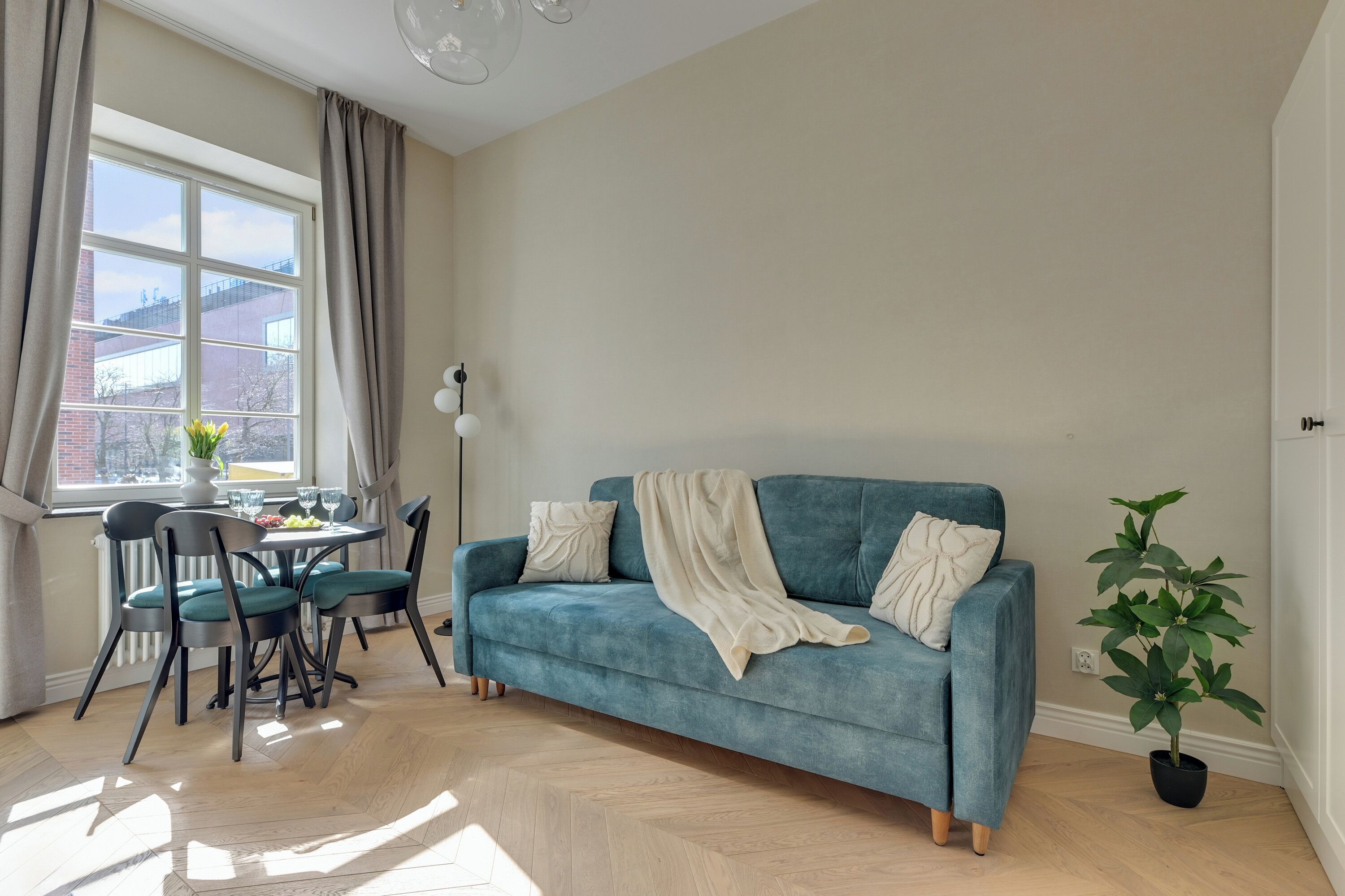 Un salon comprenant un canapé, une table à manger, des chaises, une plante en pot et une fenêtre avec des rideaux.