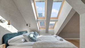 Ein Schlafzimmer mit Oberlicht, einem Bett mit weißer Bettwäsche, einem Nachttisch und einer wandmontierten Leuchte.