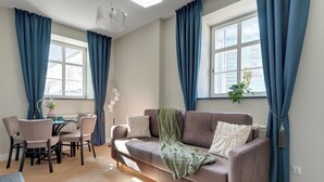 Ein modernes Wohnzimmer mit einer Couch, einem Esstisch, Stühlen und großen Fenstern mit Vorhängen.