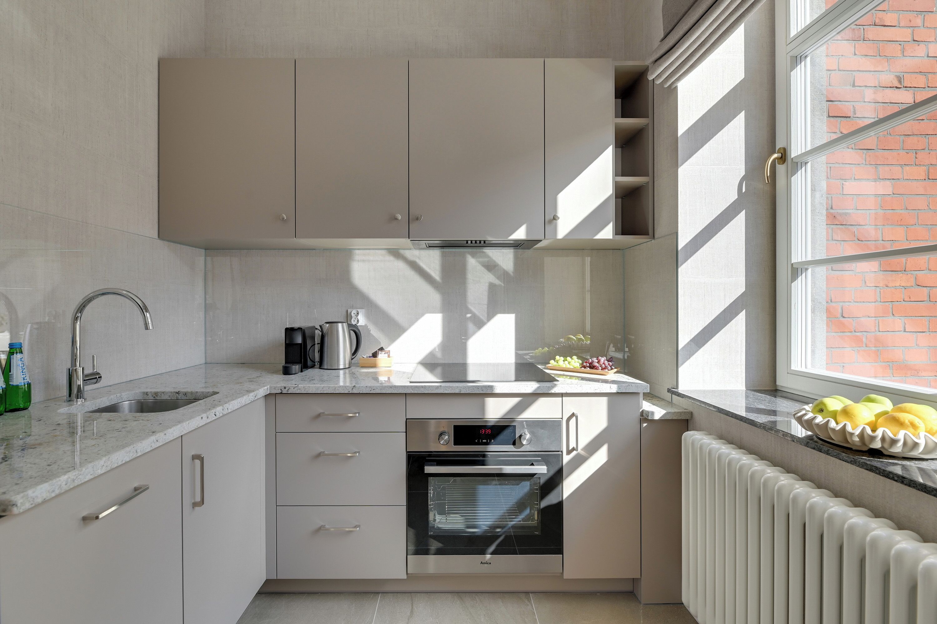Una cucina moderna con forno integrato, lavello e finestra vista su un edificio in mattoni.