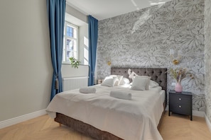 A bedroom with a bed, a nightstand, a window with curtains, and a floral wallpaper. - Budynek Dyrekcji by Browar Hevelius (Gdańsk)