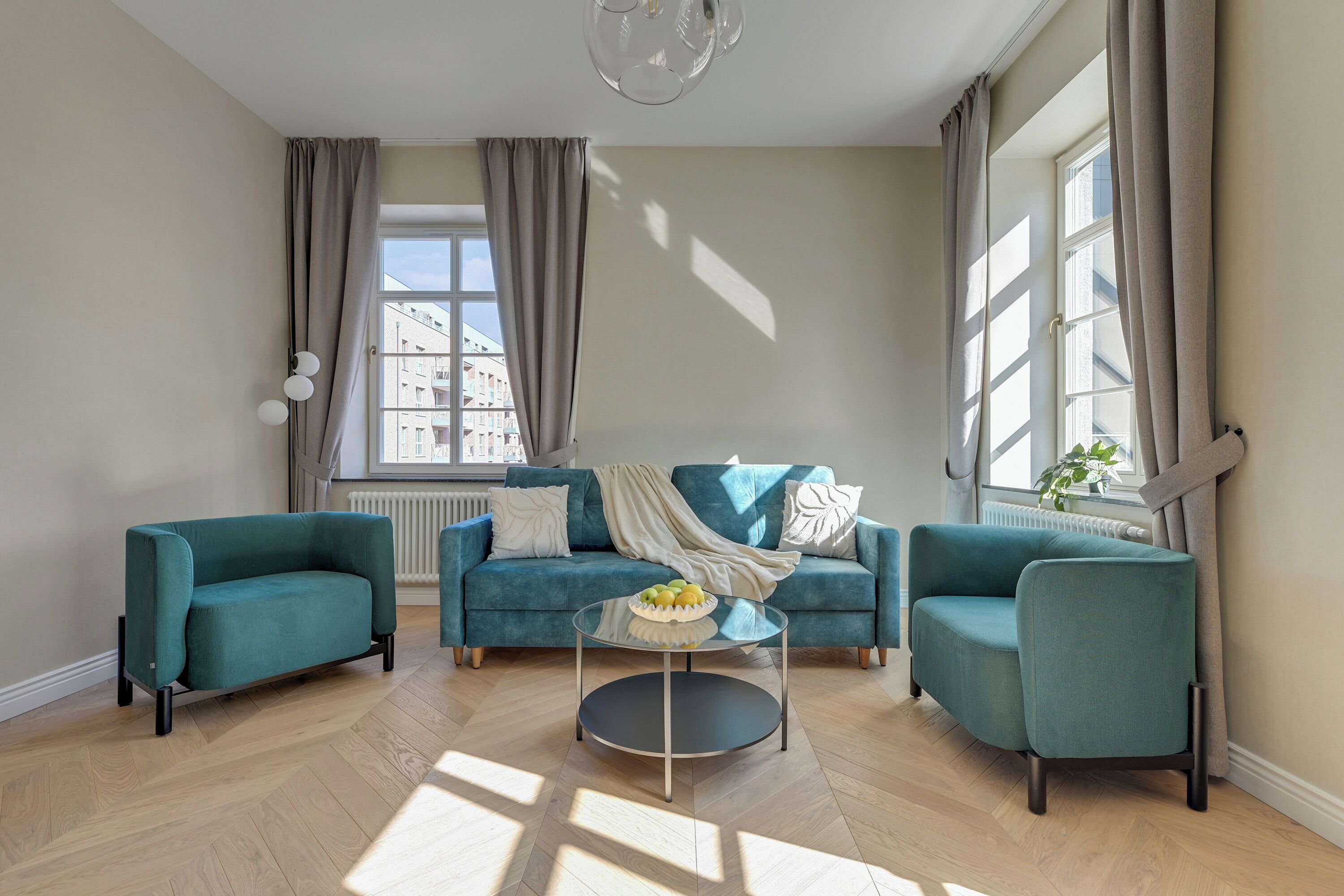 Una sala de estar moderna con un sofá turquesa, una mesa de centro redonda y ventanas amplias con cortinas.