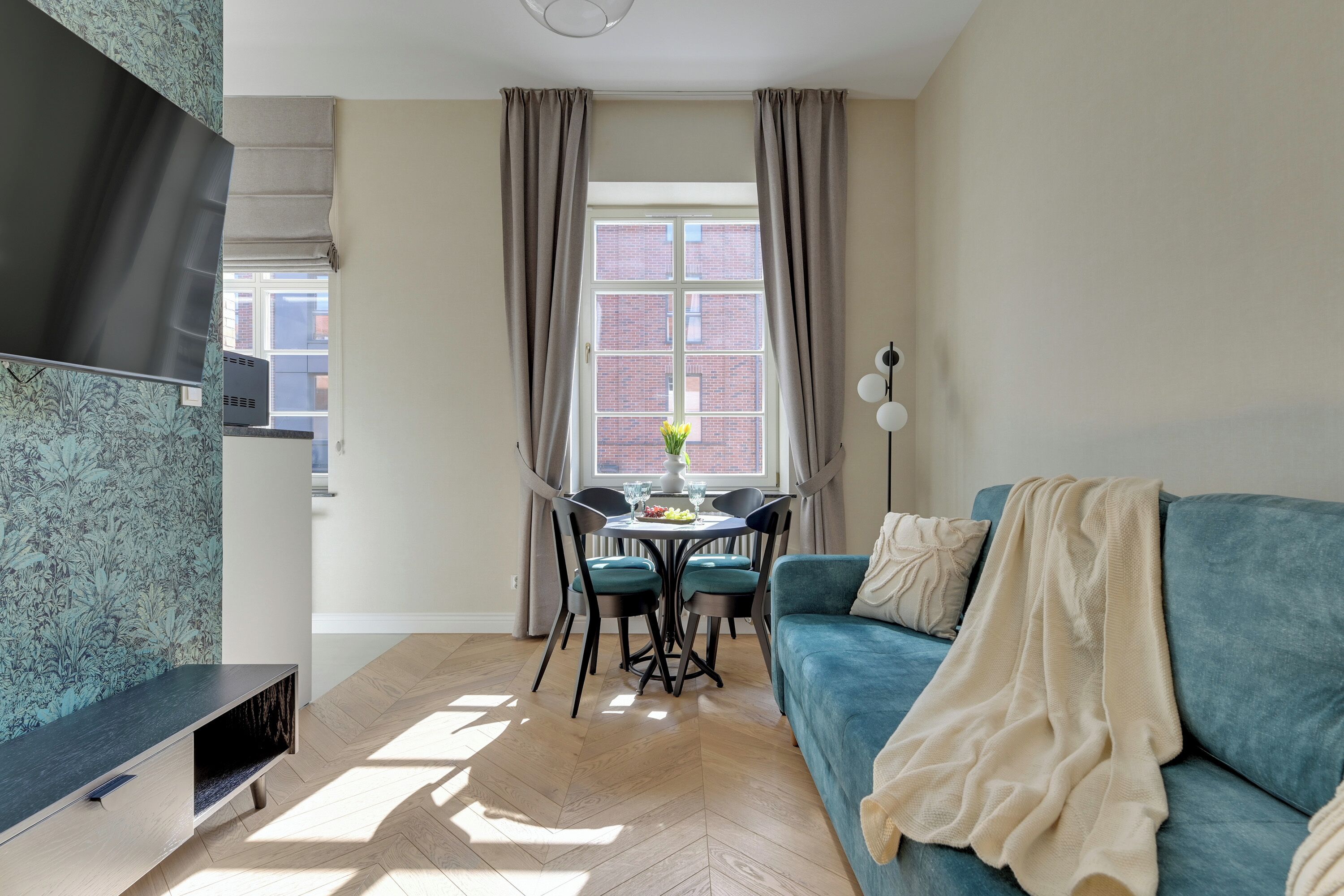 A living room with a blue sofa, a dining table with chairs, a TV, and a window with curtains.