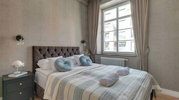 Una camera da letto con testiera trapuntata, un letto con biancheria a righe, un comodino con una lampada e una finestra con tende.