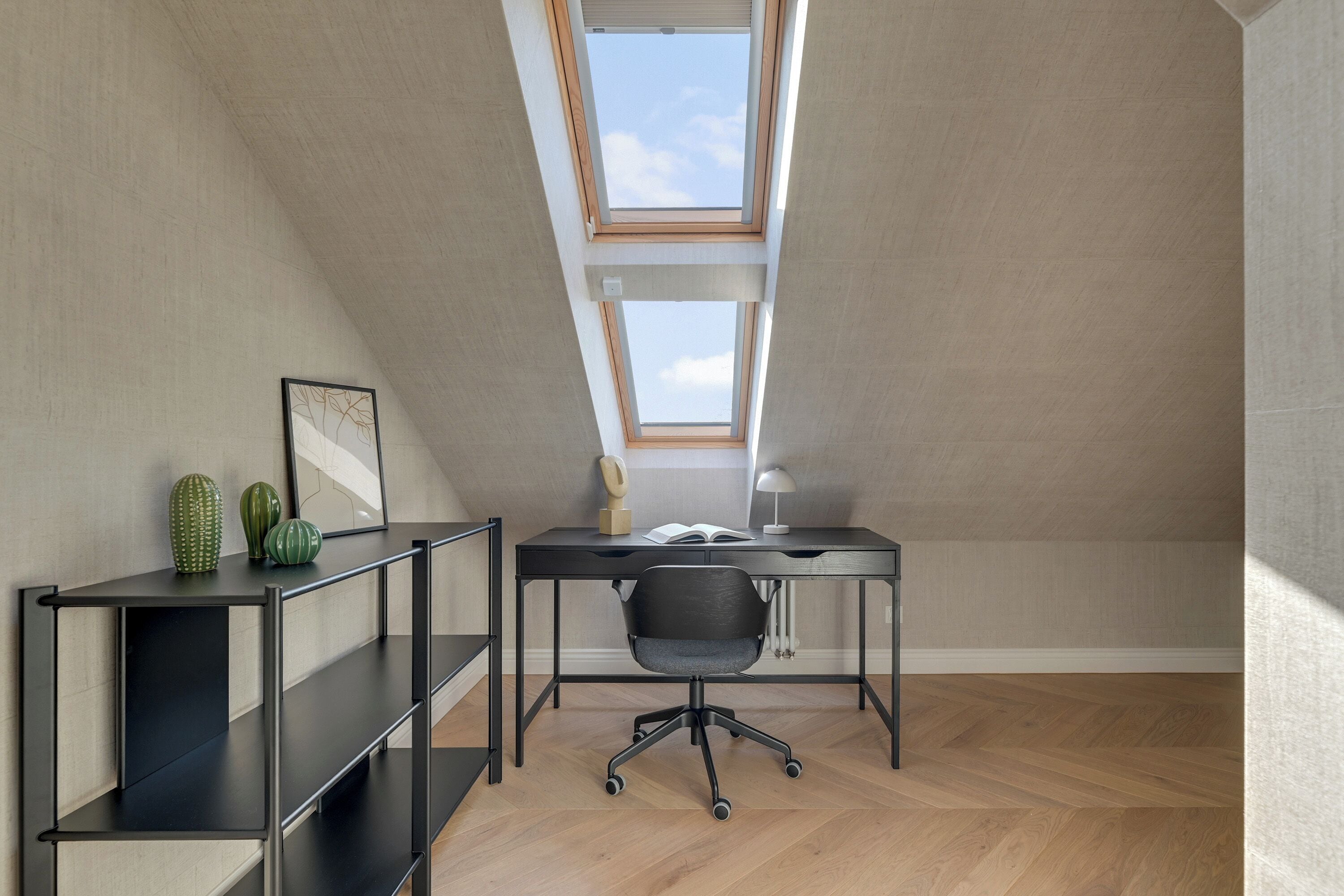 A modern attic room with a sloped ceiling, skylight, and a desk with office chair.