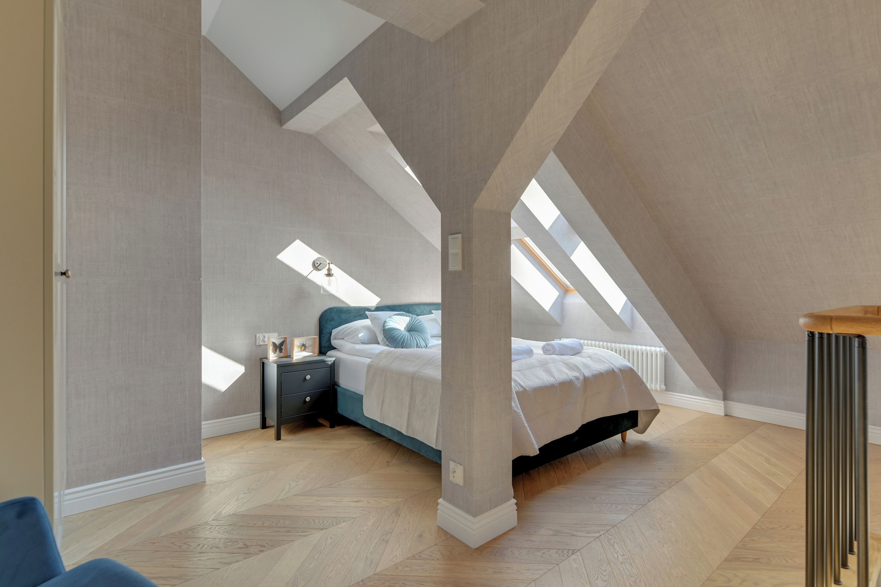 A bedroom with a sloped ceiling, a bed with a blue headboard, a nightstand, and a radiator.