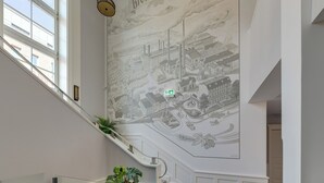 Ein Wandgemälde zeigt eine städtische Szene mit einer Treppe und einer Pflanze auf der Brüstung.