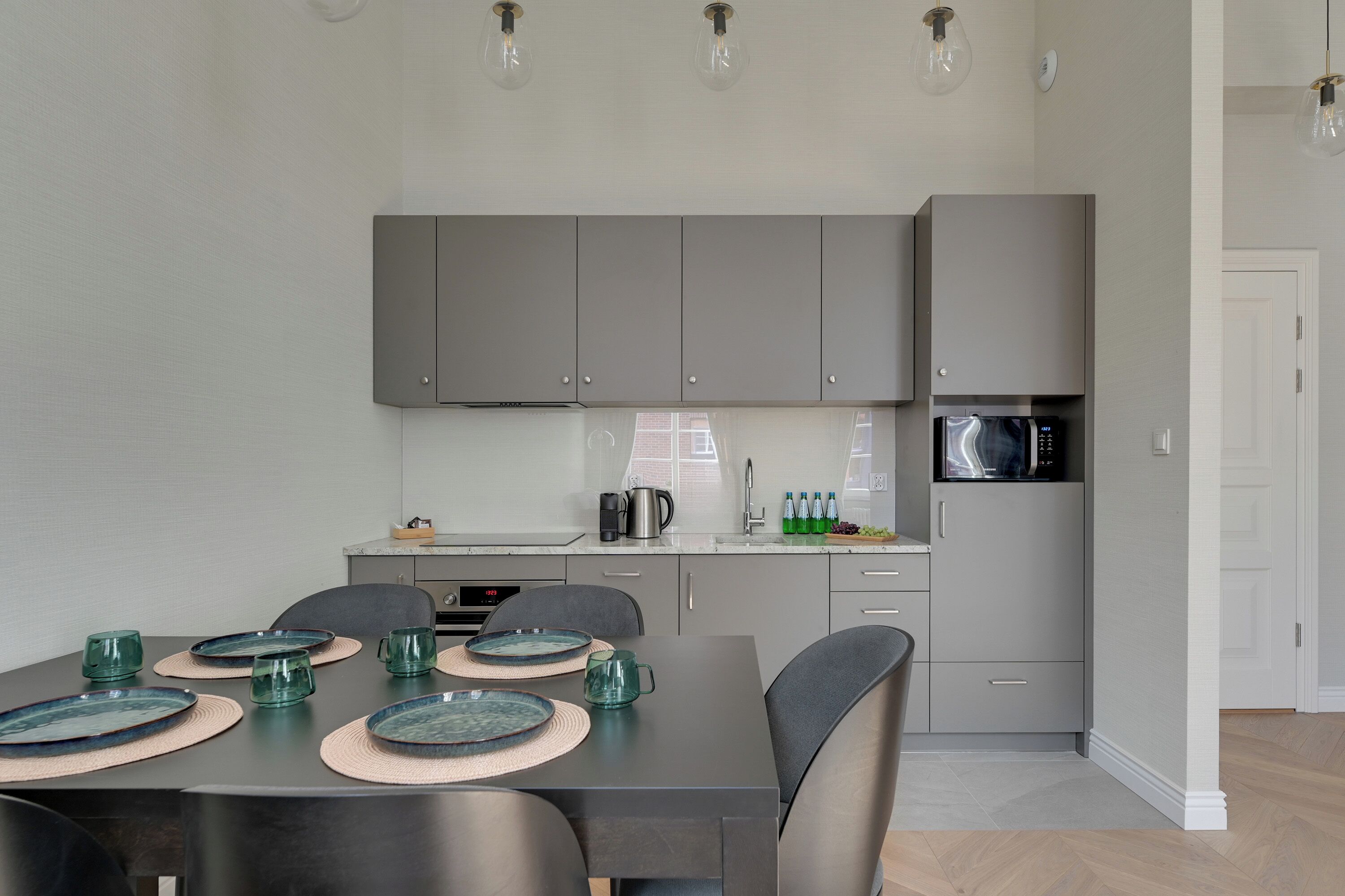 Una cocina moderna con armarios grises, una mesa de comedor con platos y vasos, y un microondas.
