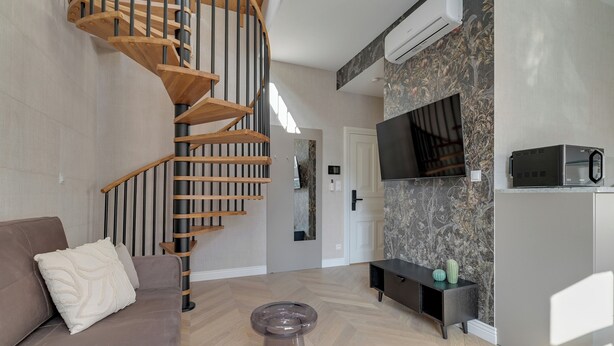 Ein modernes Wohnzimmer mit einer Wendeltreppe aus Holz, einer Couch, einem Couchtisch, einem an der Wand montierten Fernseher und einer Mikrowelle in einem Schrank.