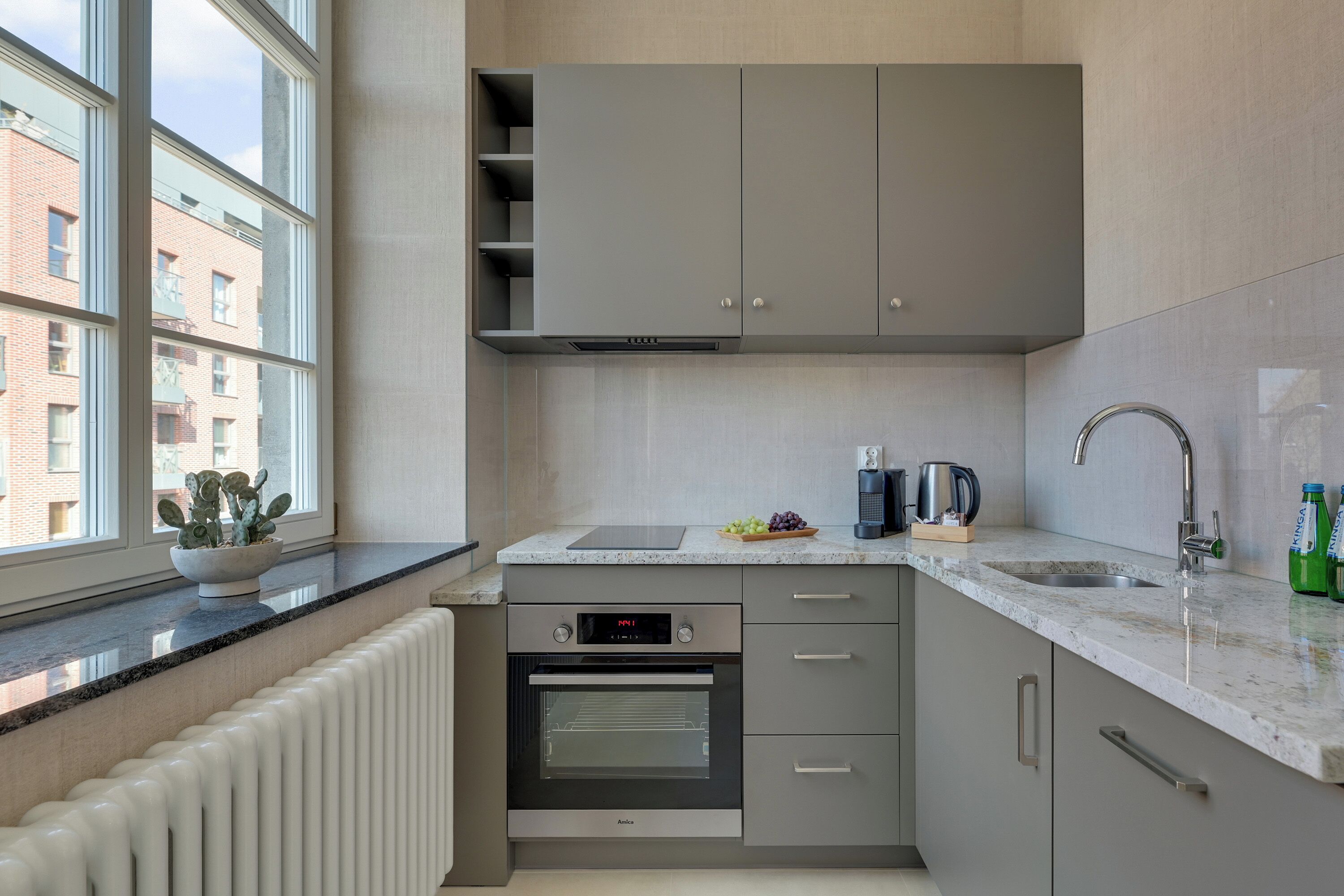 Una cucina moderna con forno integrato, una finestra vista edifici e un piano di lavoro con elettrodomestici.
