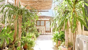 Un espacio al aire libre cubierto con plantas en macetas, un portón de madera y una unidad de aire acondicionado.