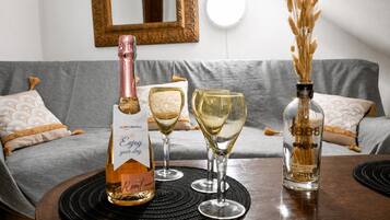 Una botella de vino, dos copas de vino y un jarrón decorativo sobre una mesa en una habitación con un sofá gris y un espejo en la pared.
