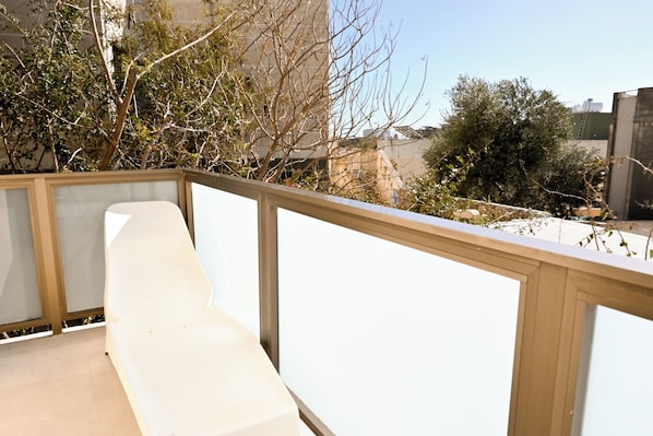 A balcony with a white chair, a wooden railing, and a view of buildings and trees. - Sefranda Guesthouse Ensuite Rooms (St. Julian's)