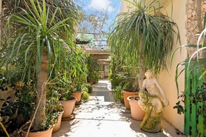 A narrow pathway flanked by potted plants and a statue, leading to a building with a green roof. - Sefranda Guesthouse Ensuite Rooms (St. Julian's)