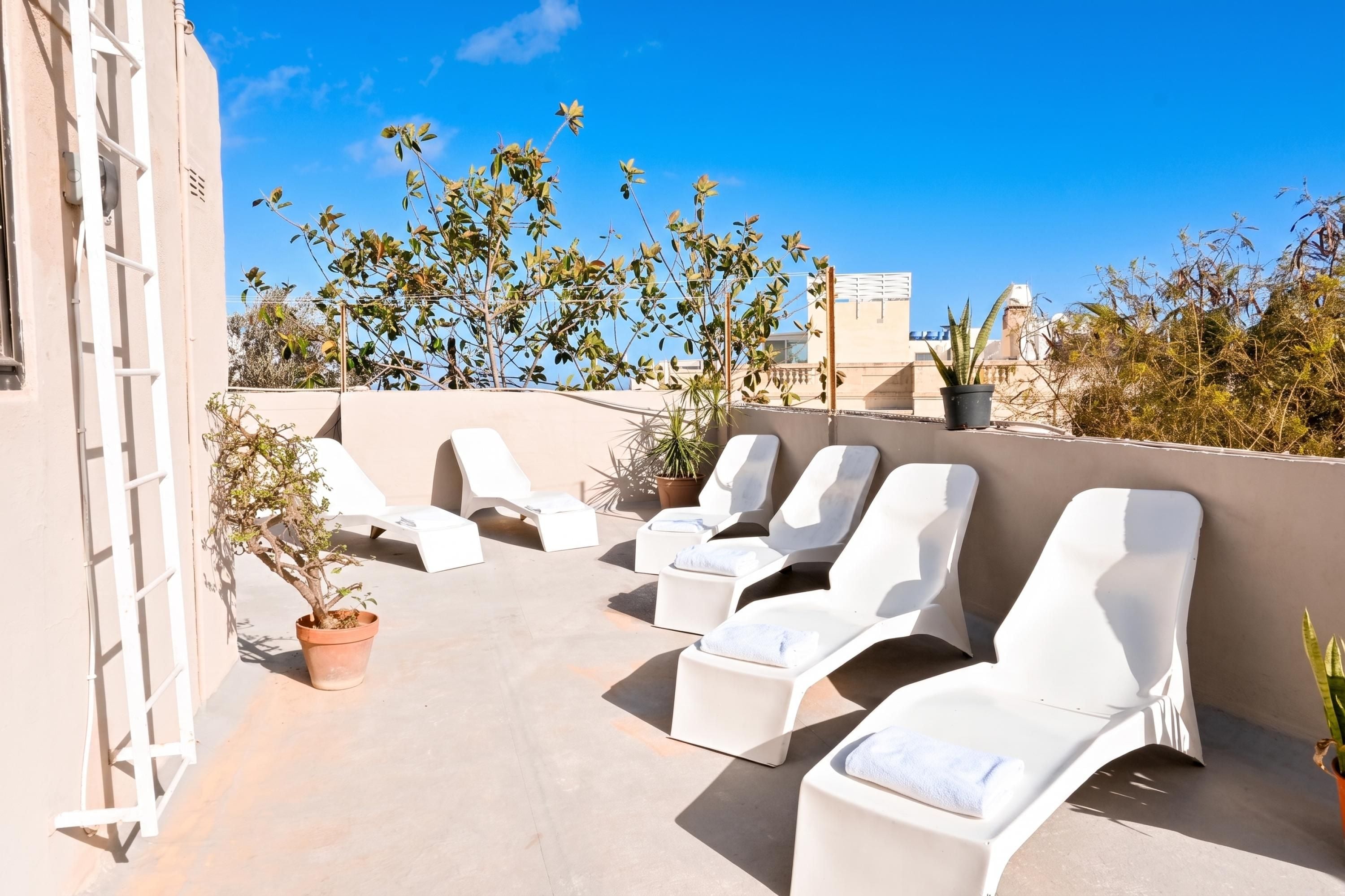 A rooftop terrace with white lounge chairs and potted plants.