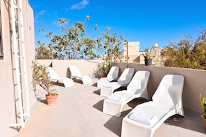 Terraza en la azotea con sillones blancos y plantas en macetas.