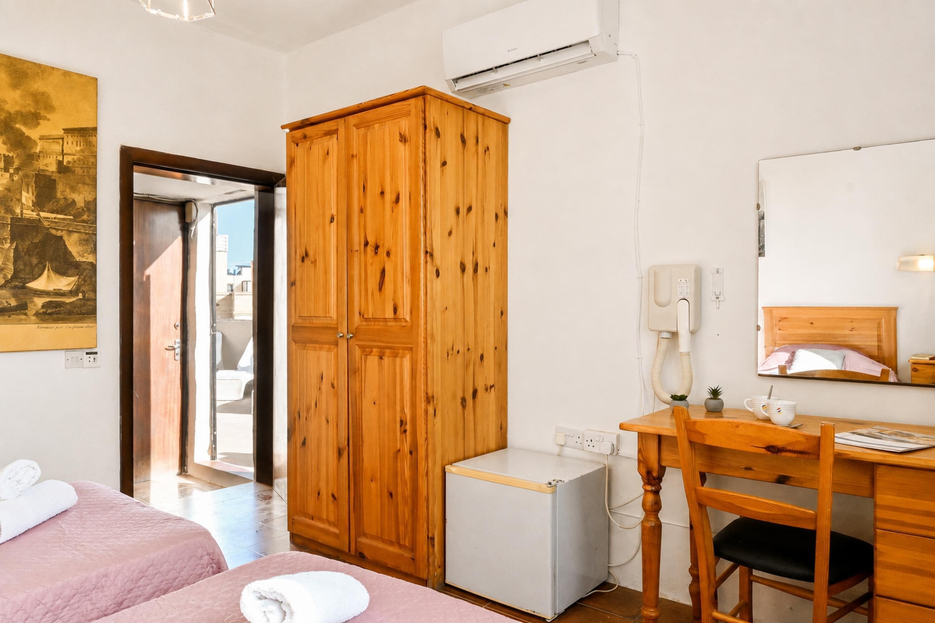 Un dormitorio con dos camas, un armario de madera, un escritorio con silla y un refrigerador pequeño.