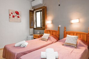 A hotel room with two beds, a window with wooden shutters, a bedside table with a lamp, and a wall-mounted air conditioner. - Sefranda Guesthouse Ensuite Rooms (St. Julian's)