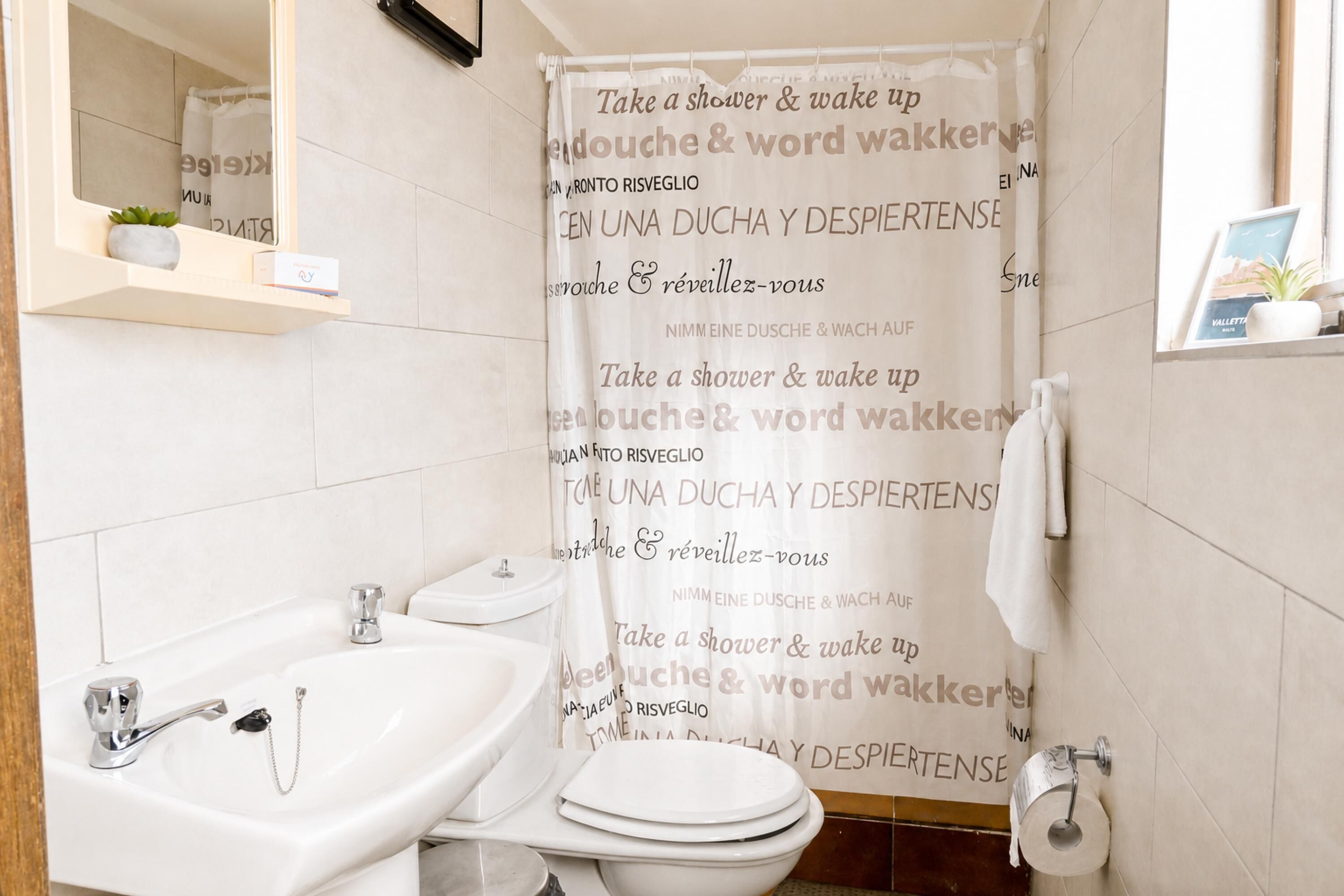 A bathroom with a shower curtain featuring text in multiple languages, a white sink, and a toilet.