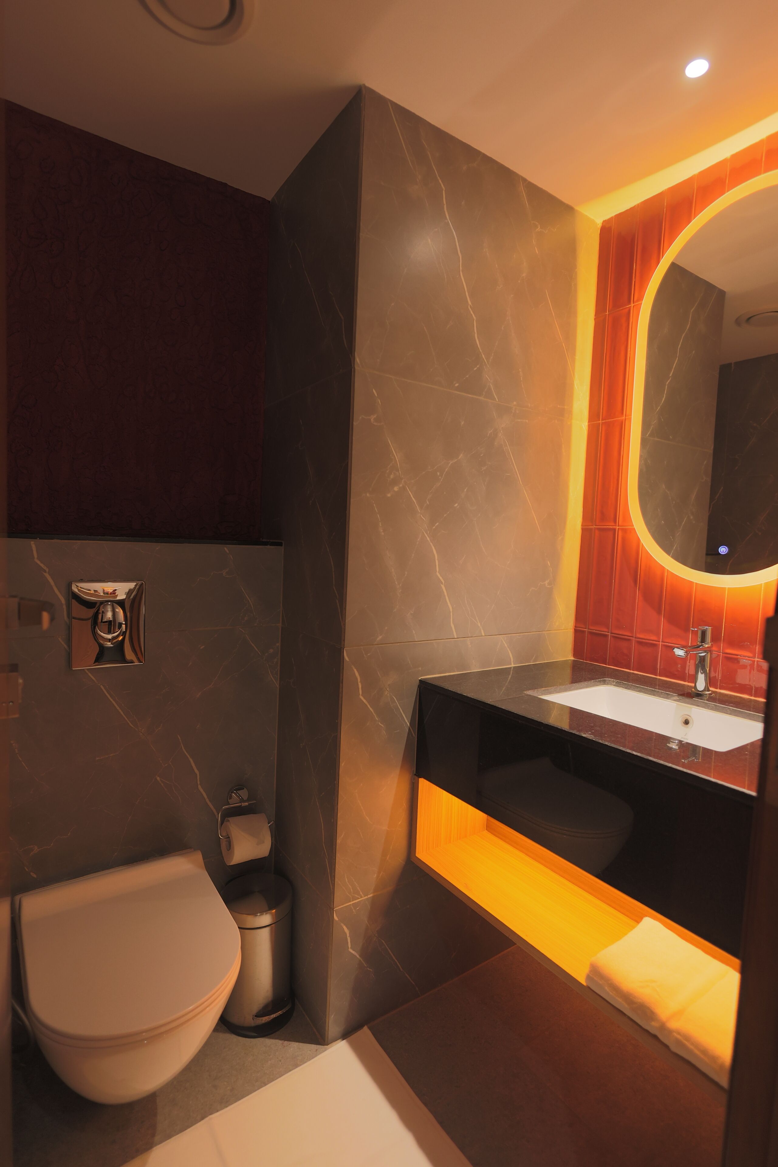 A modern bathroom with a marble sink, a toilet, and a mirror with a warm light.