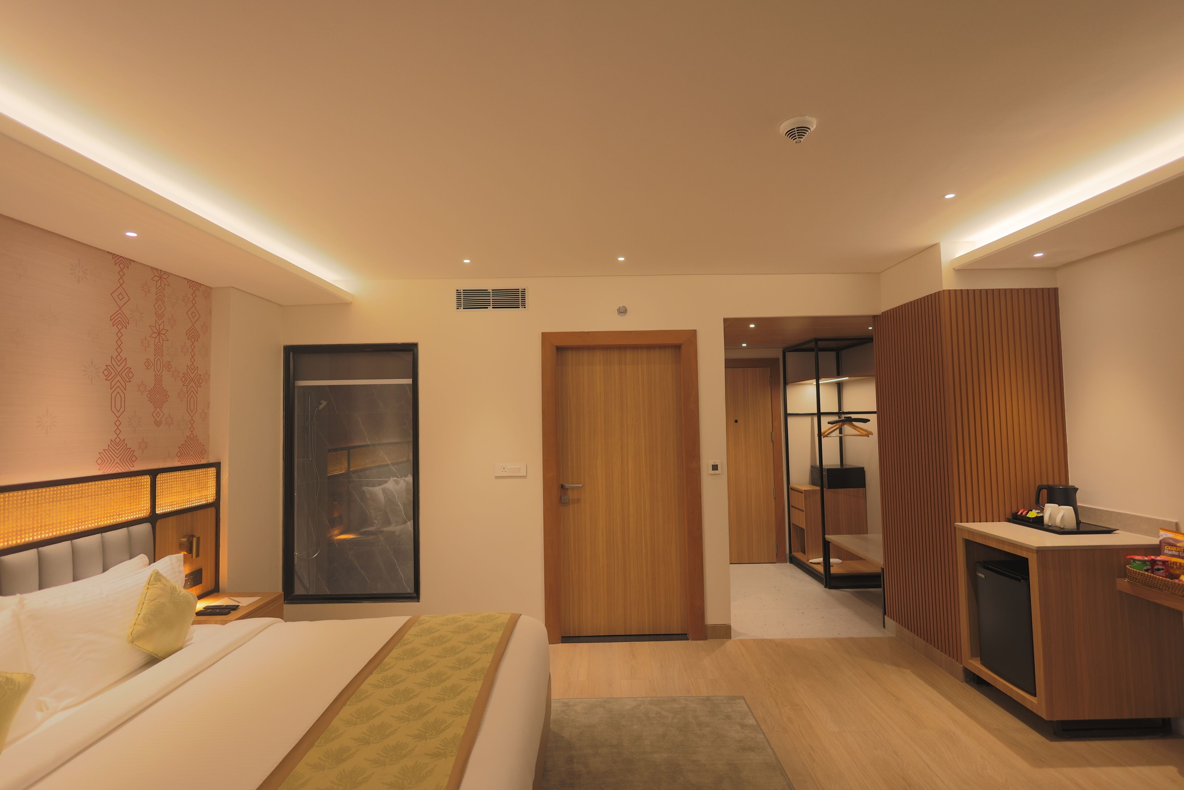 A modern hotel room with a bed, a desk, a wardrobe, and a bathroom visible through an open door.