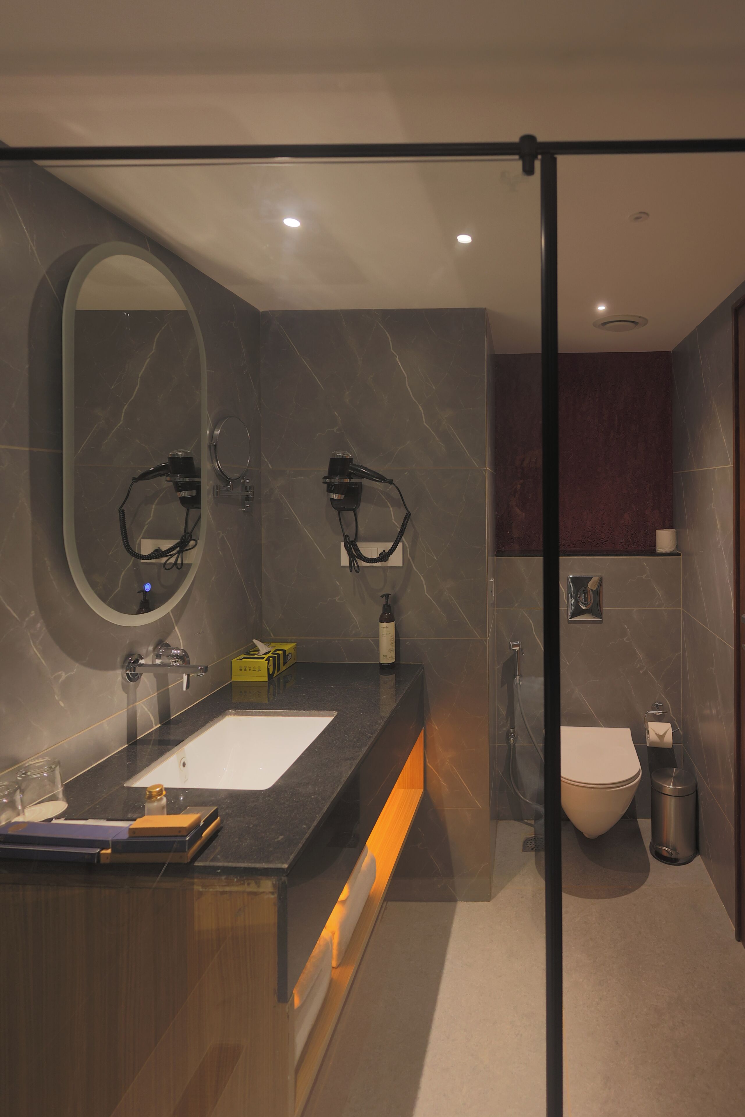 A modern bathroom with a marble vanity, a large mirror, a toilet, and a glass shower enclosure.
