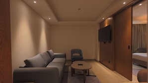 A modern hotel room with a sofa, a small table, a chair, a TV, and a sliding door leading to a bed. - Hotel Palacio Paltan Bazaar (Guwahati)