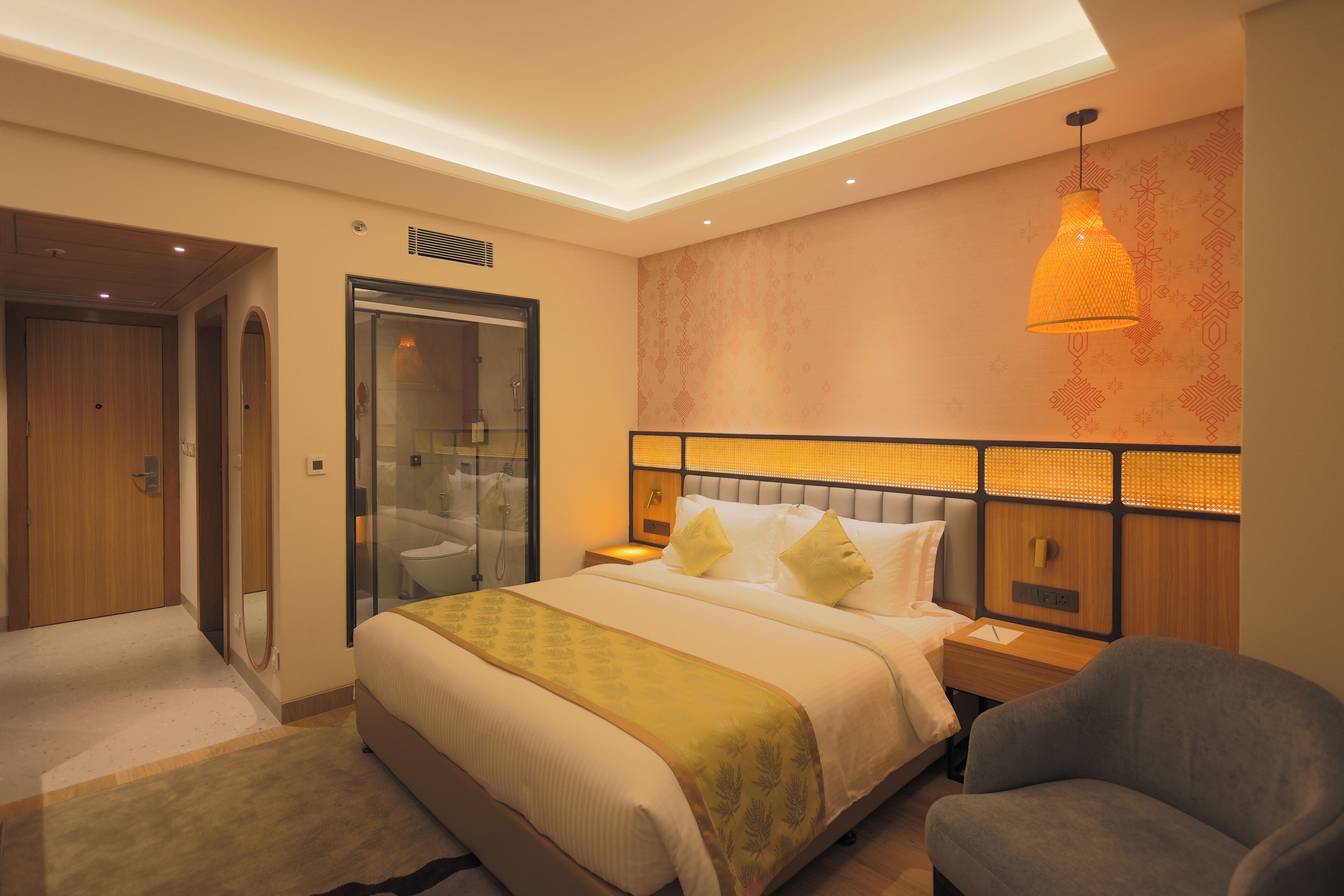 A hotel room with a large bed, a bedside table, a chair, a glass shower enclosure, and a patterned wall.