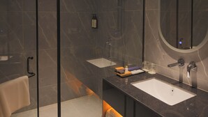 A modern bathroom with a glass shower enclosure, a large mirror, and a marble-tiled wall. - Hotel Palacio Paltan Bazaar (Guwahati)