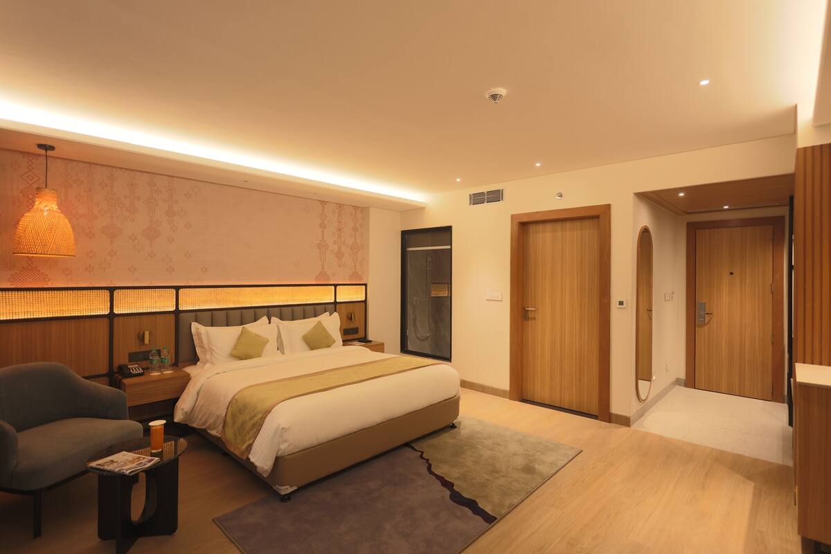 A modern hotel room with a large bed, bedside tables, a desk, a chair, and a wardrobe.