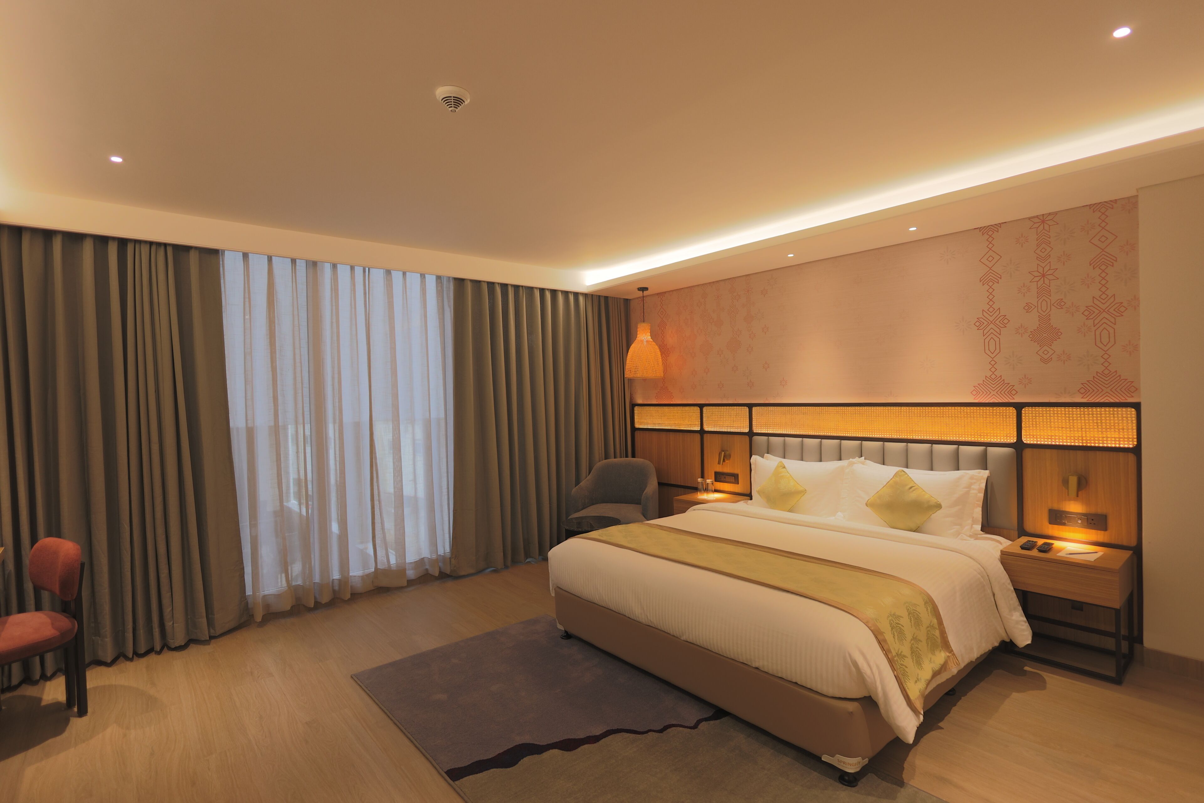 A hotel room with a large bed, a chair, a bedside table, and a lamp.