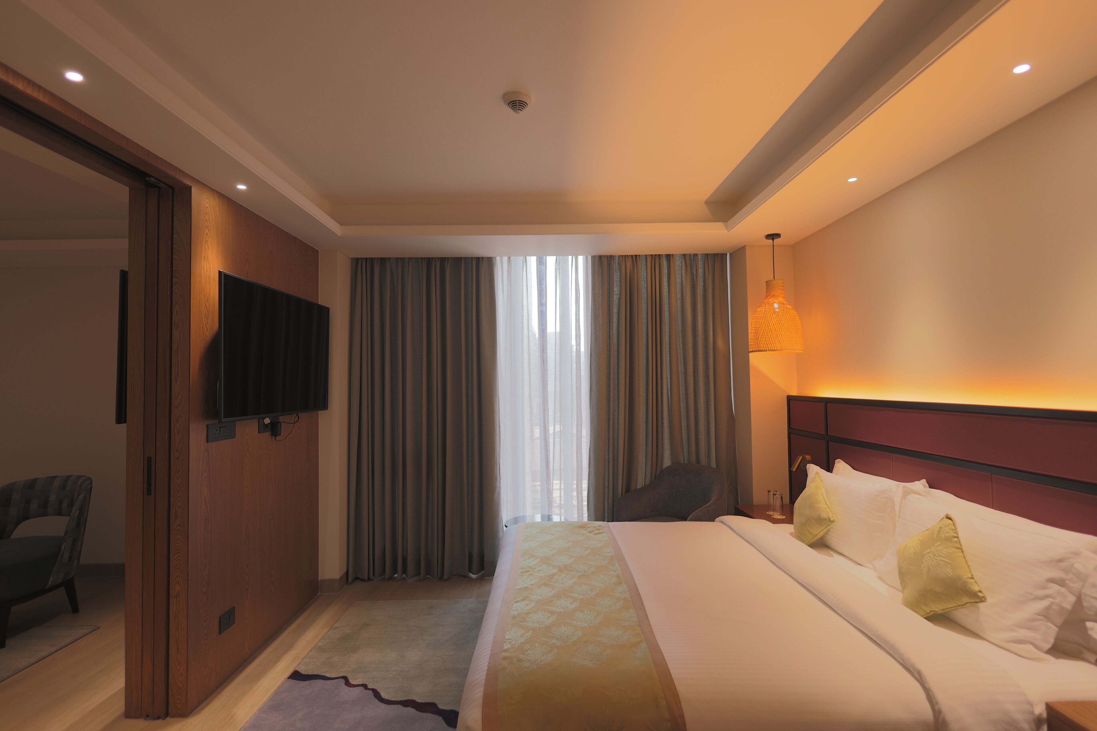 Una habitación de hotel con cama, cortinas, televisor, una silla y lámpara.