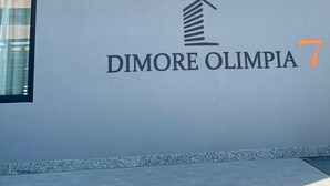 Un immeuble avec une enseigne indiquant « DIMORE OLIMPIA 7 » et présentant un design architectural moderne.