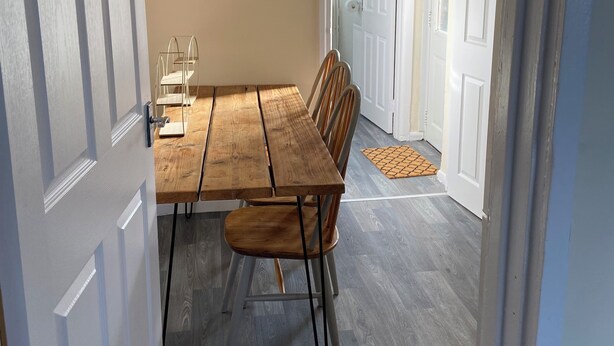 Un coin repas avec une table et des chaises en bois, un mur de couleur claire et une porte donnant sur une autre pièce.